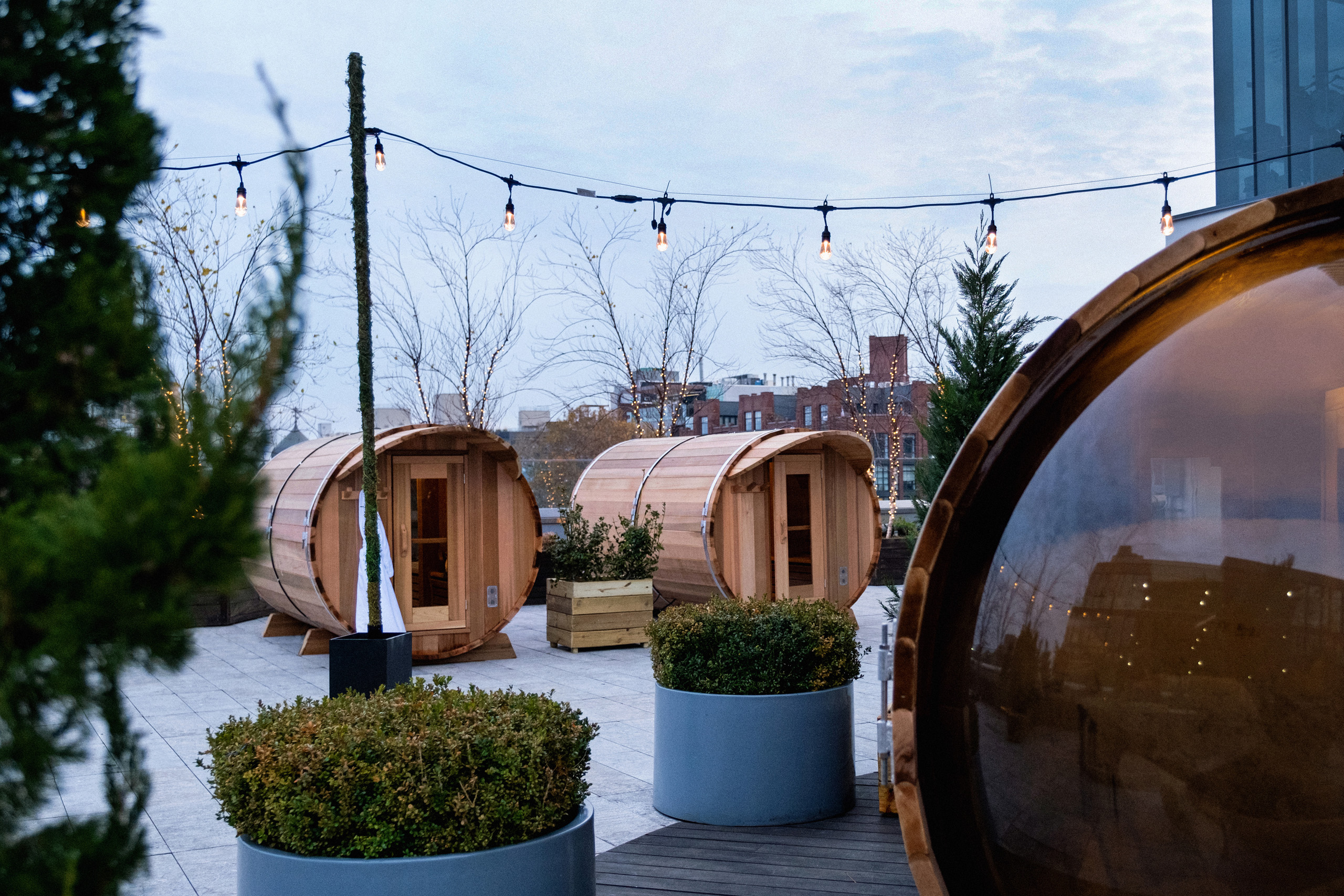 Outdoor barrel saunas on a rooftop surrounded by potted plants.