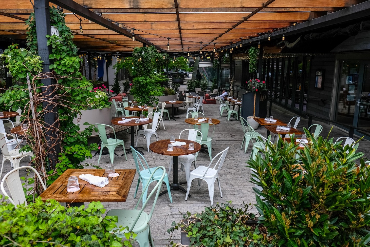 Outdoor patio dining with wooden tables and greenery.