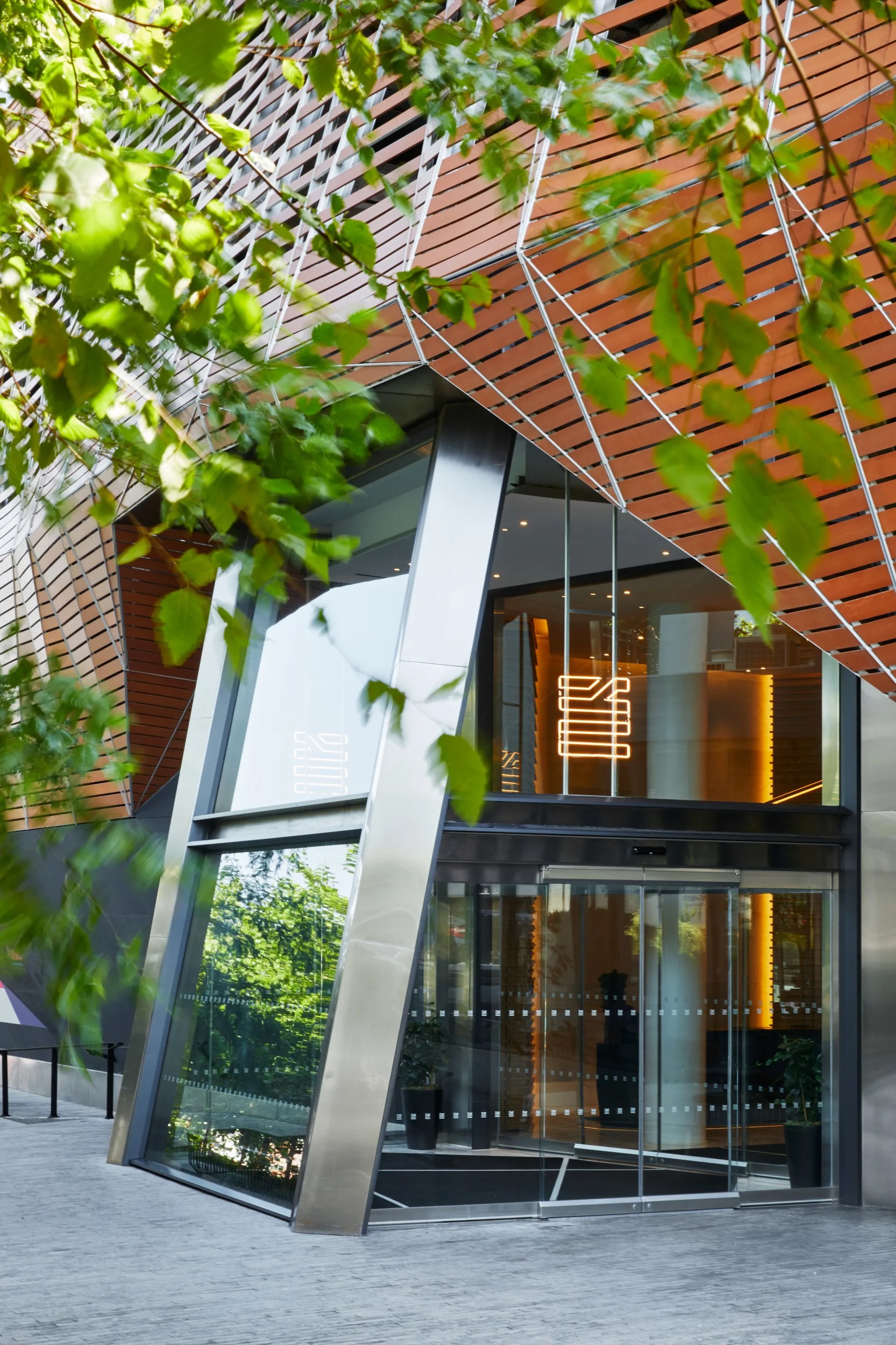 Modern glass hotel entrance framed by greenery and wood panels.