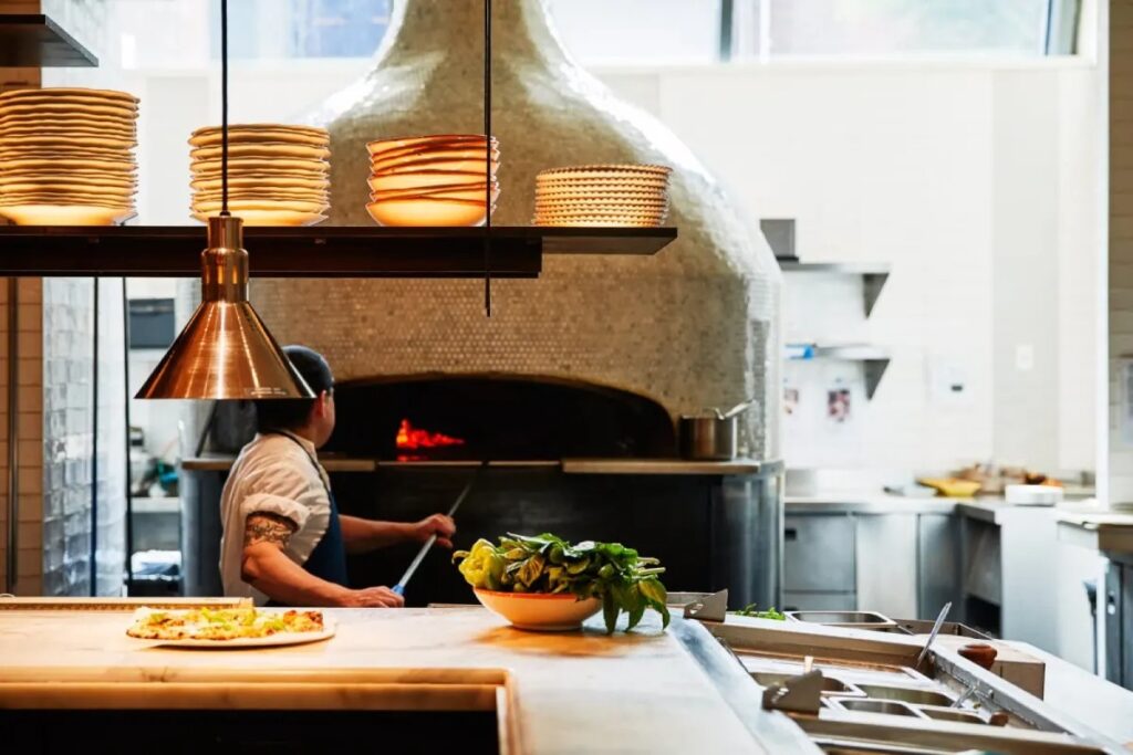 Chef placing pizza in wood-fired oven under warm lighting.