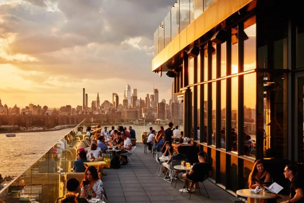 Rooftop restaurant with people dining at sunset skyline view.