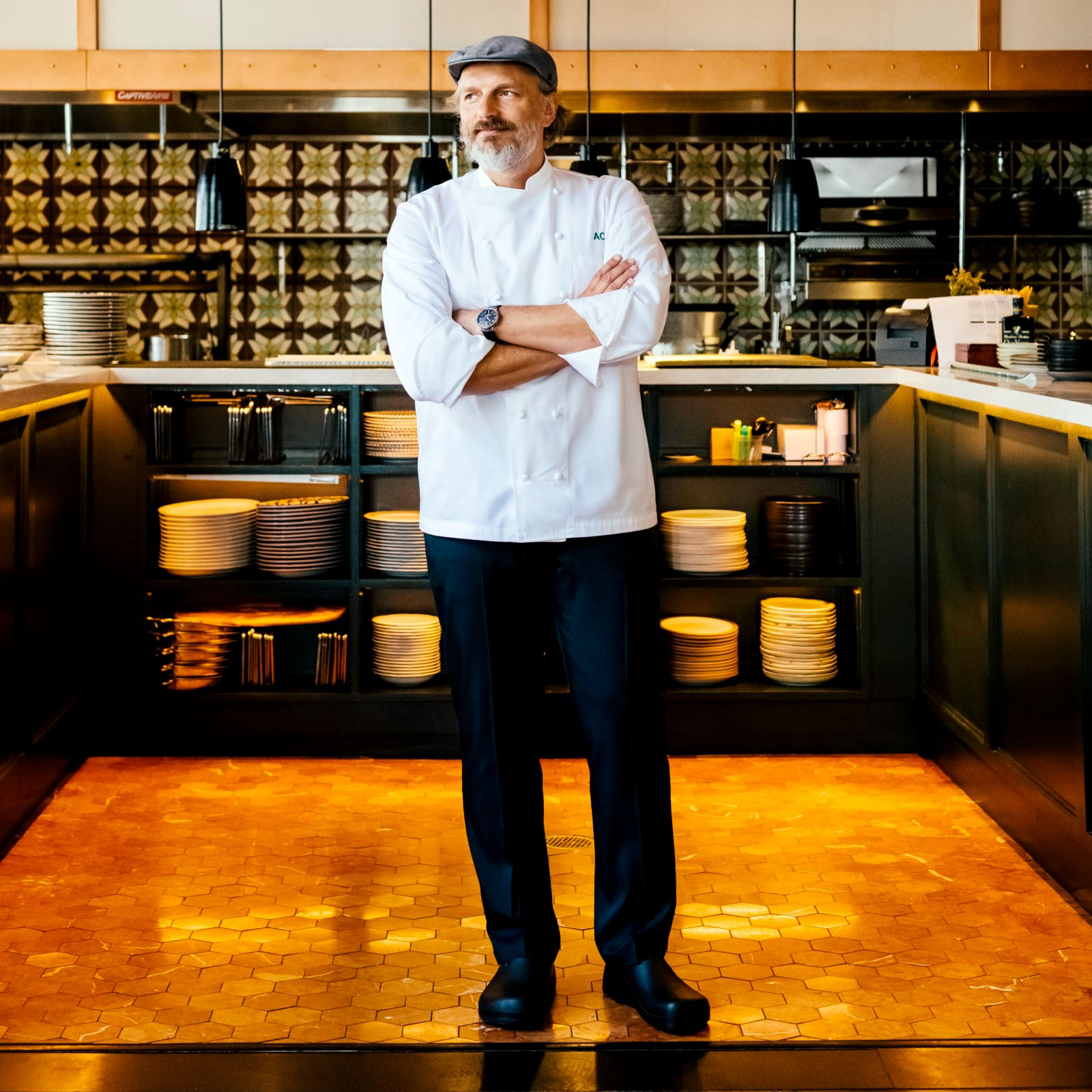 Chef in white coat standing confidently in a modern kitchen.