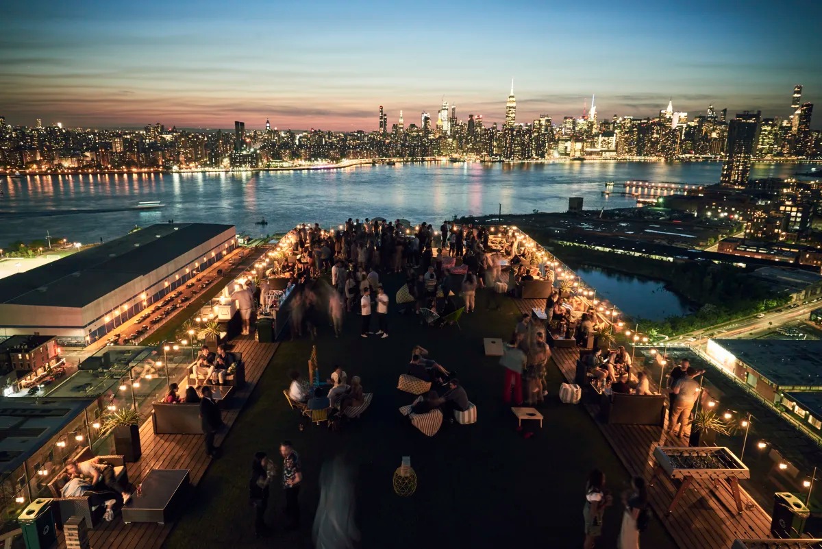 Nighttime rooftop gathering with string lights and city skyline.