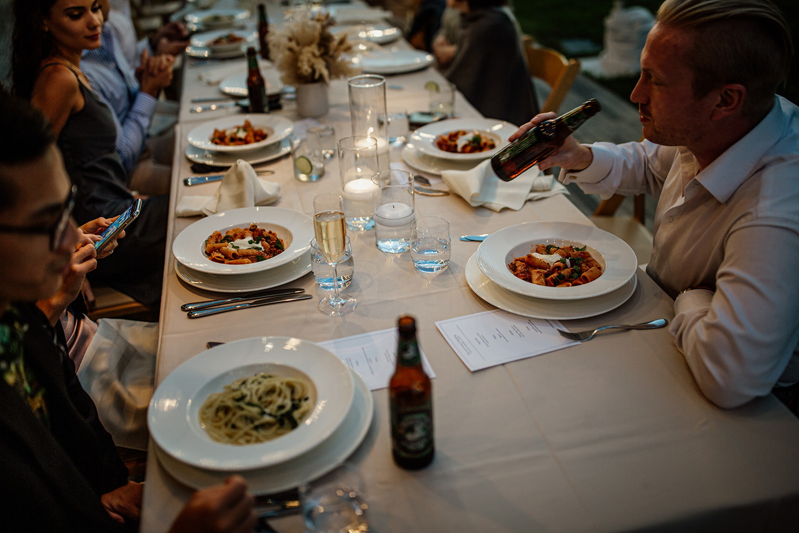 Guests dining outdoors with pasta and wine.