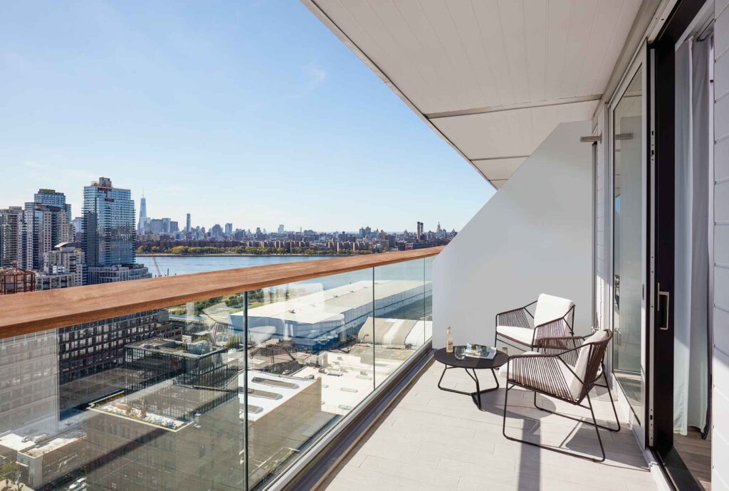Balcony with city skyline view, two chairs, and table.
