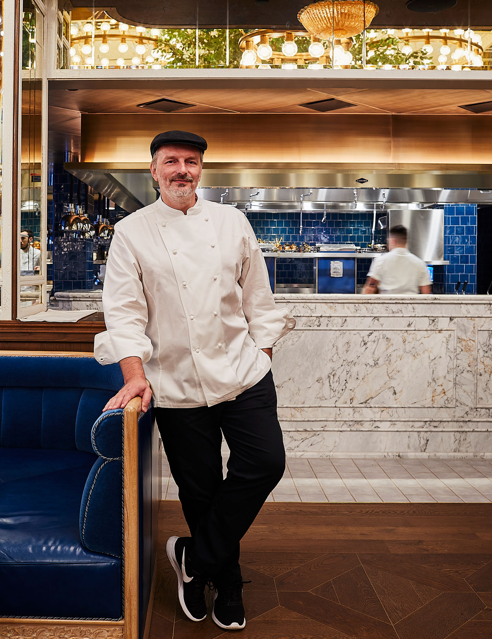 Chef Carmellini in a white kitchen smock standing confidently infront of the kitchen