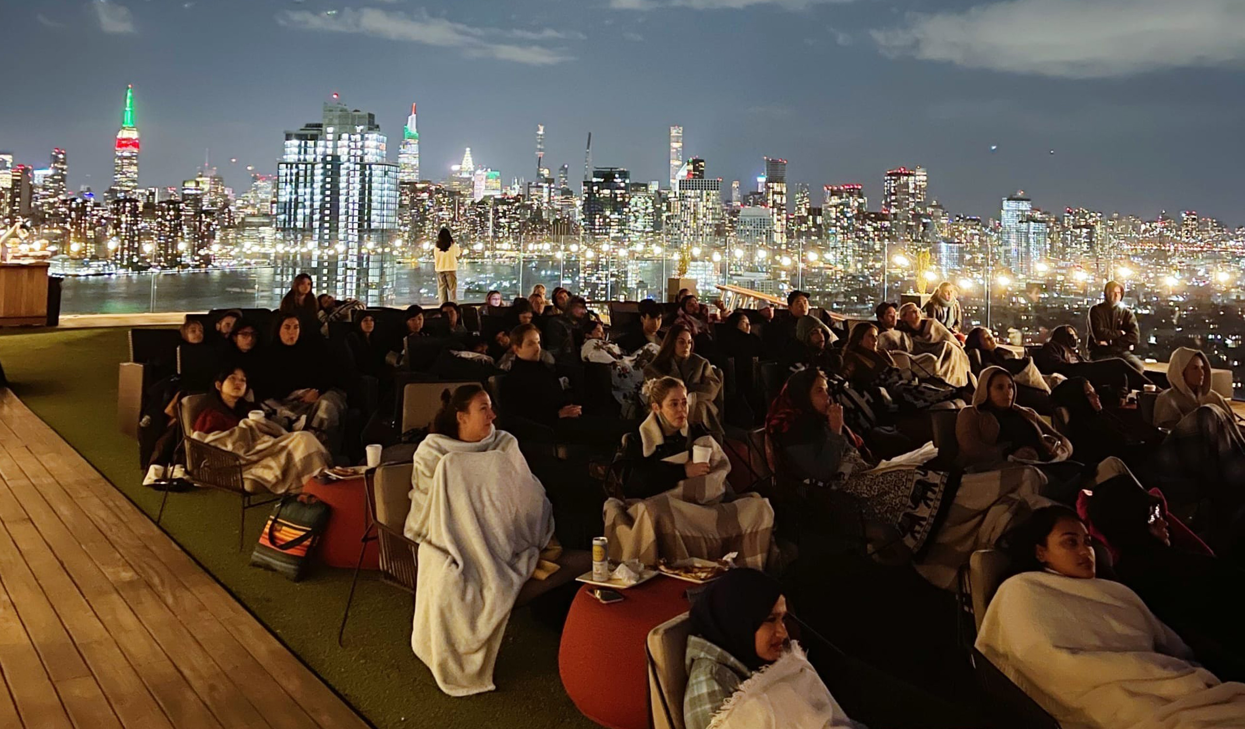 Crowd watching outdoor movie with city skyline at night.