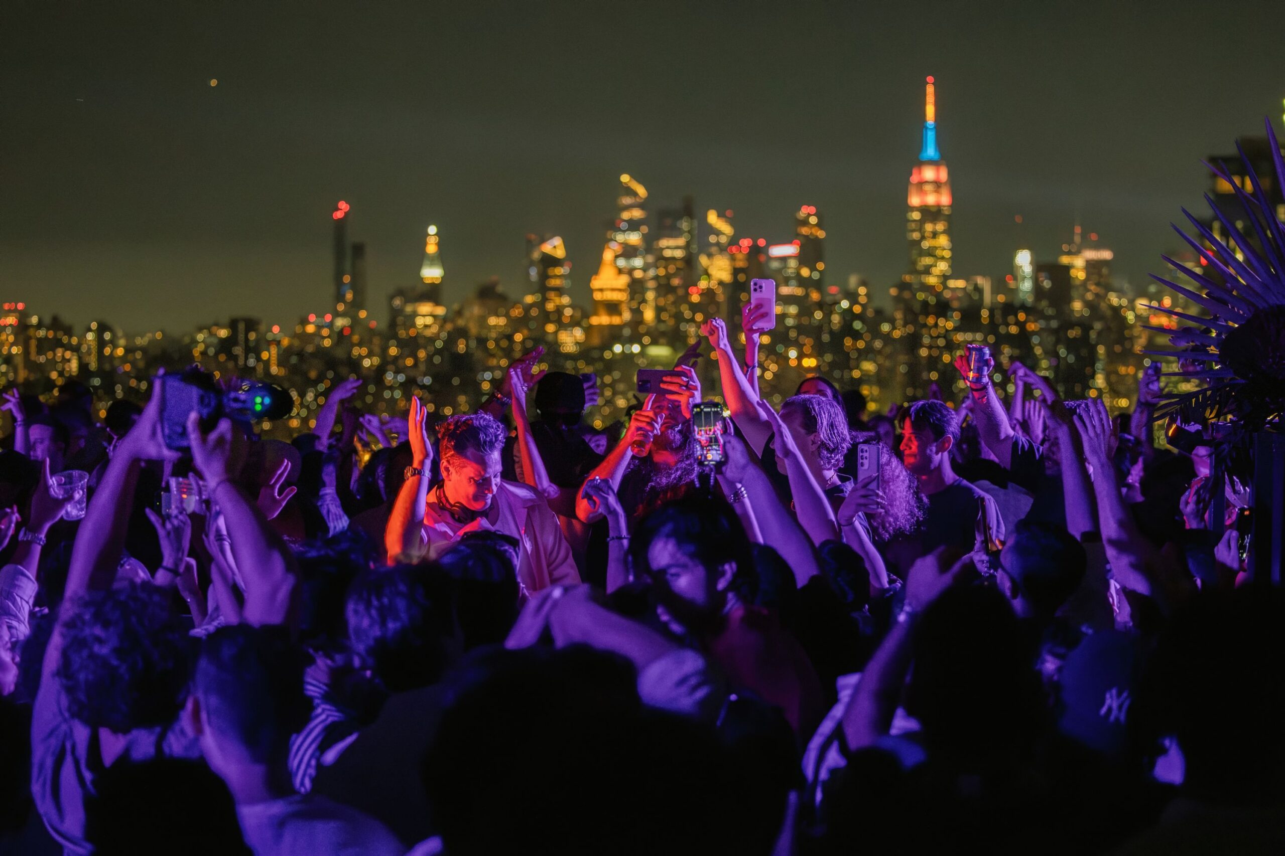 Guests dance on rooftop at party with Manhattan skyline in distance.