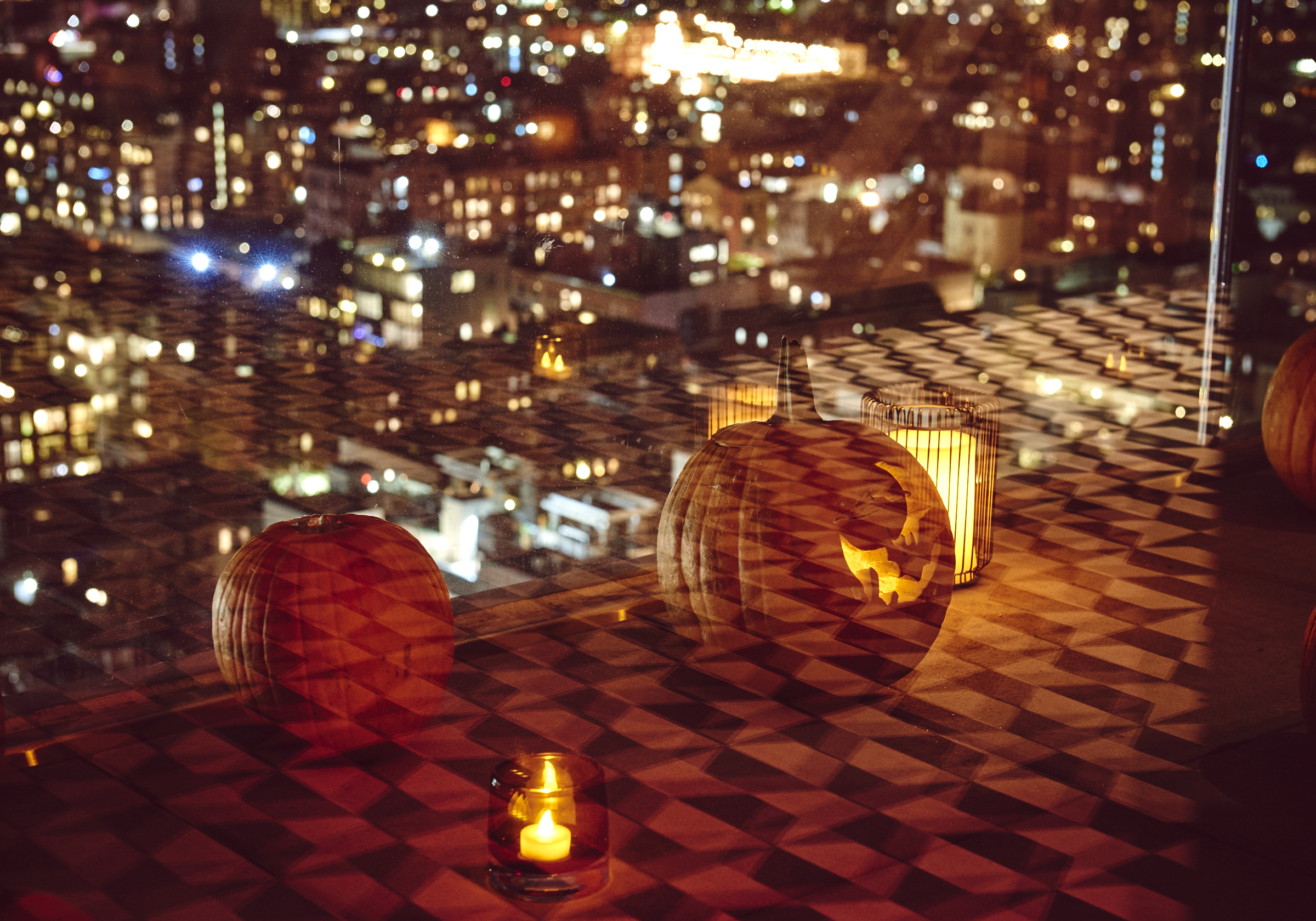 Jack-o-lanterns glow on elevator landing with the city in the background.