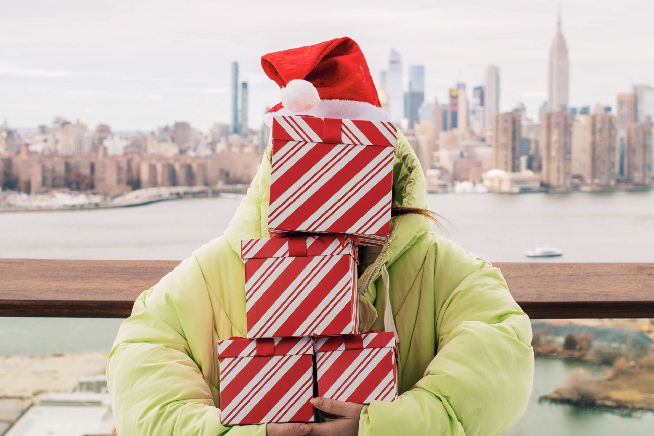 Guest in Santa hat holds several gifts on the balcony with the Manhattan skyline in the distance.