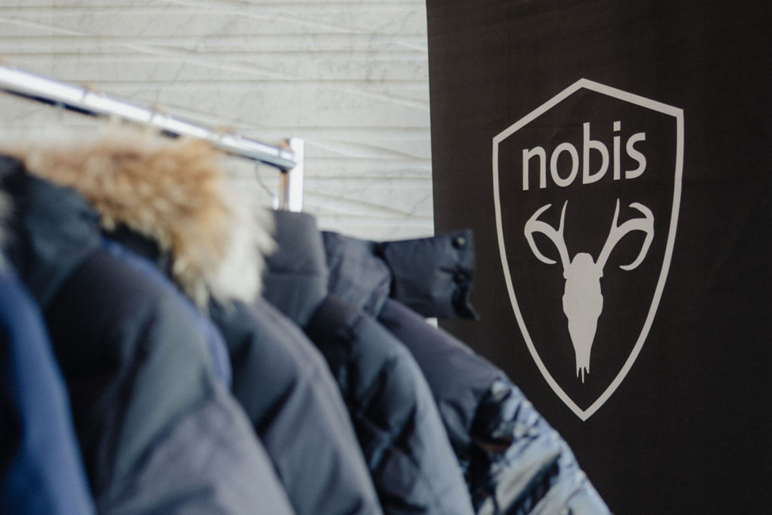 Nobis coats hang on coat rack beside Nobis signage.