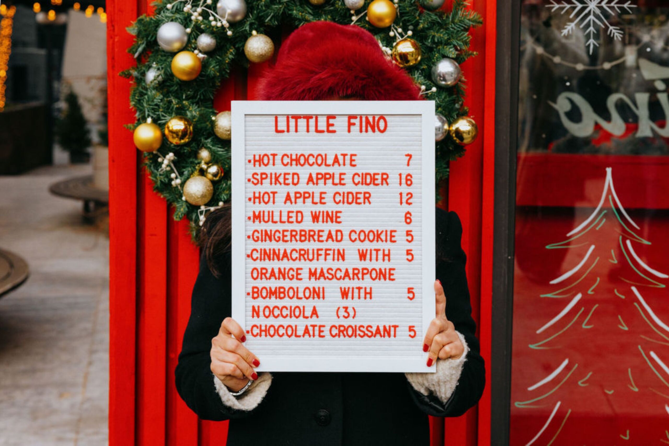 Server holds menu board in front of Little Fino holiday pop-up chalet.