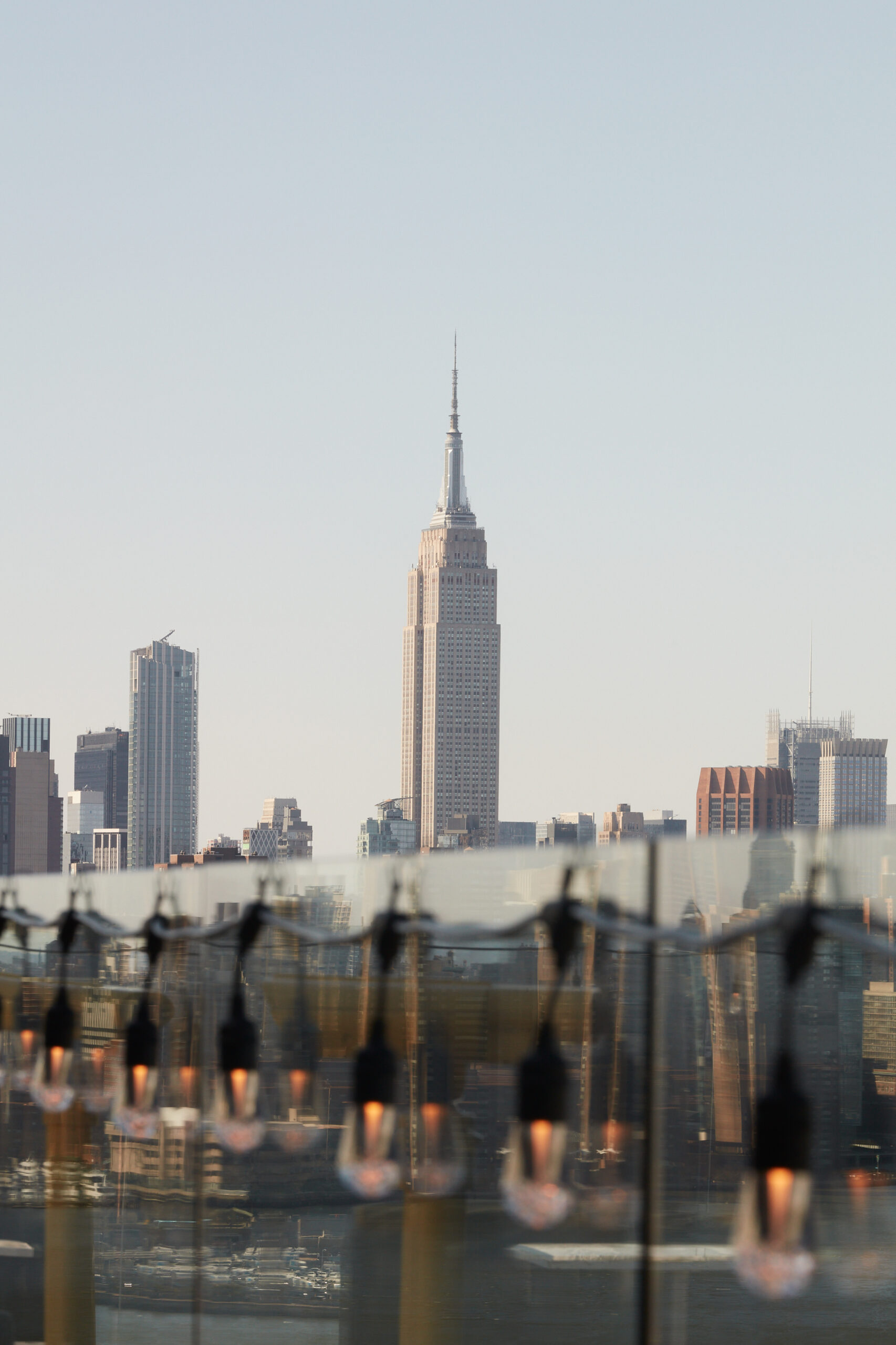 Lights hang on rooftop of The William Vale. The Empire State Building stands centered in the distance.