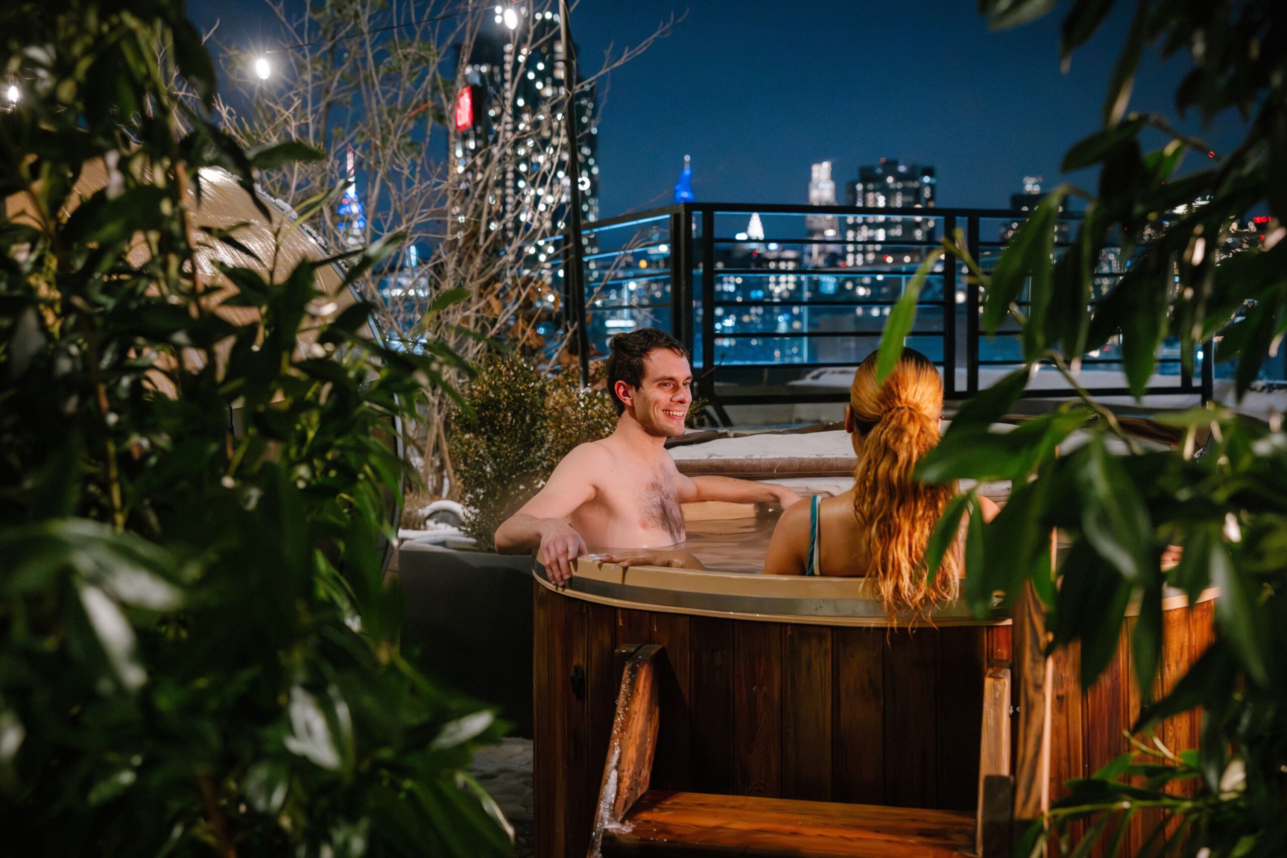Two guests relax in hot tub with Manhattan views in the distance.