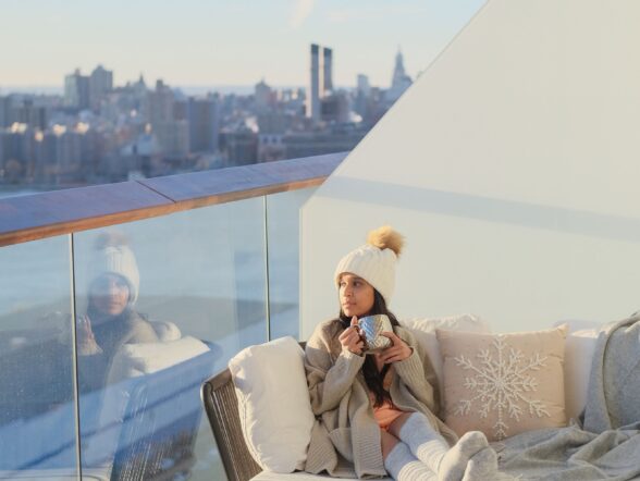 Guest sits on private balcony enjoying skyline views while cozied up sipping on a hot beverage.