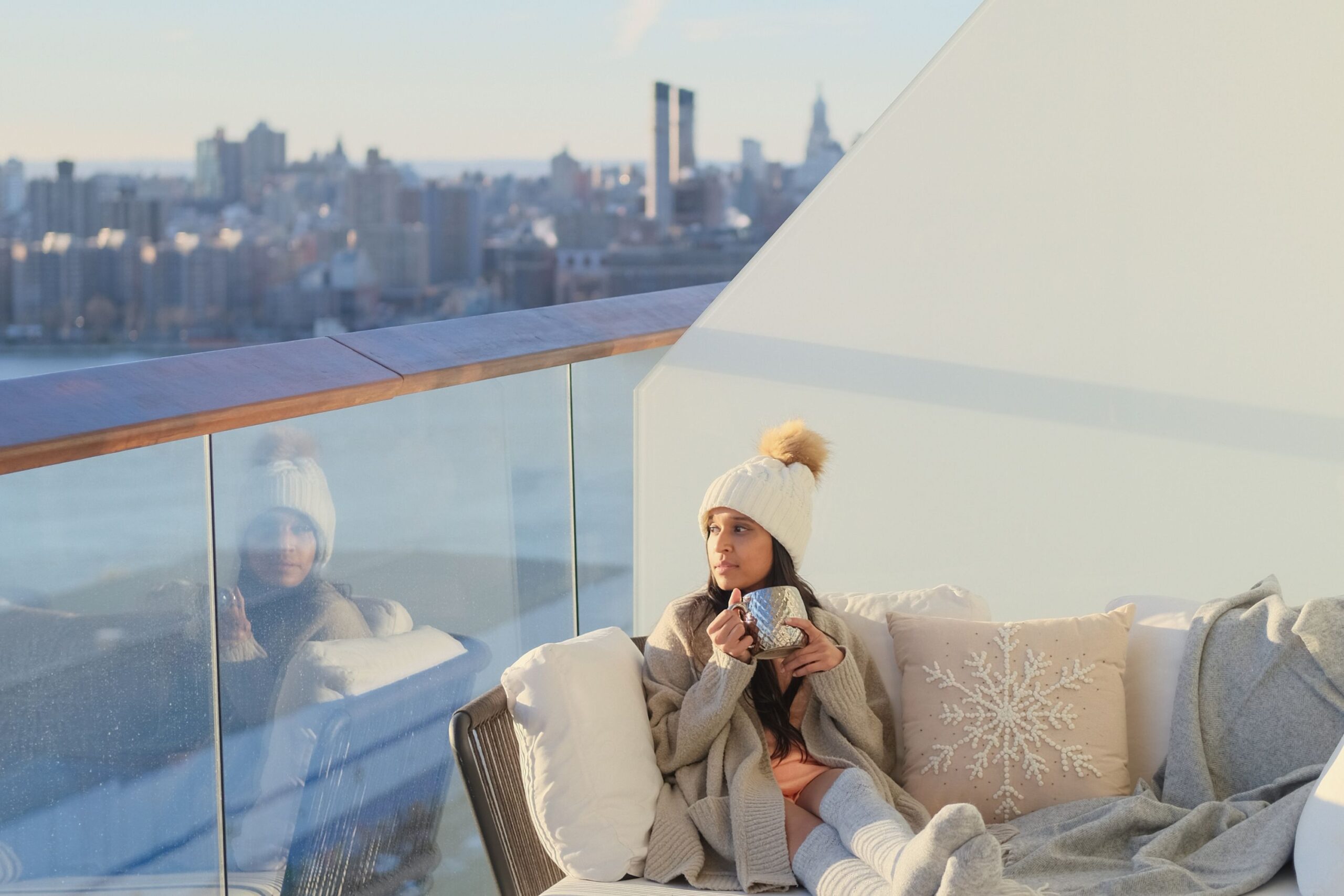 Guest sits on private balcony enjoying skyline views while cozied up sipping on a hot beverage.