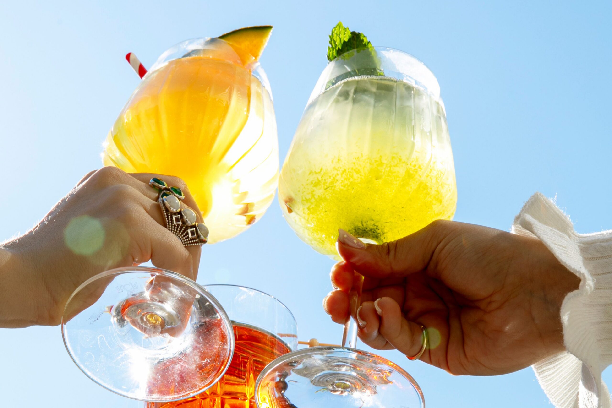 Guests clink drink glasses in the sunlight.