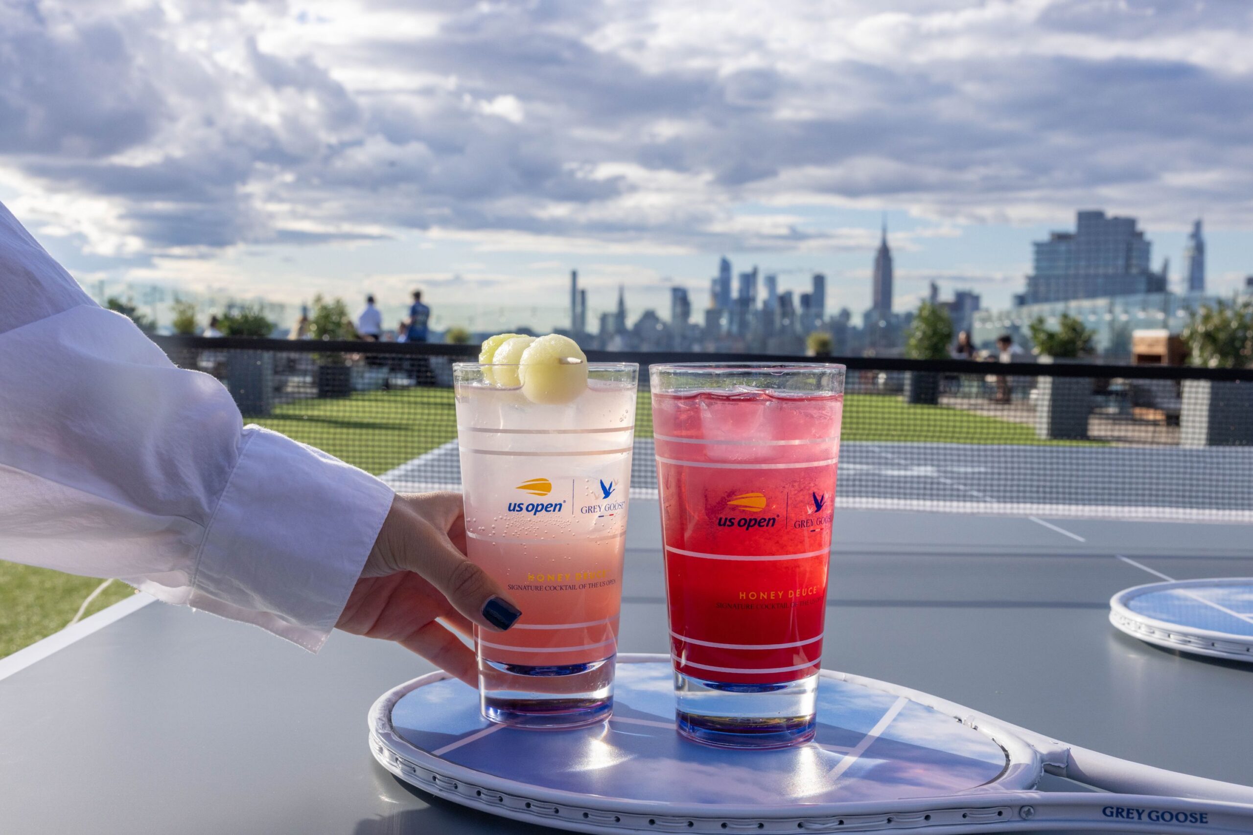 Guest grabs a honey deuce off of a racket with the Manhattan skyline in the distance.